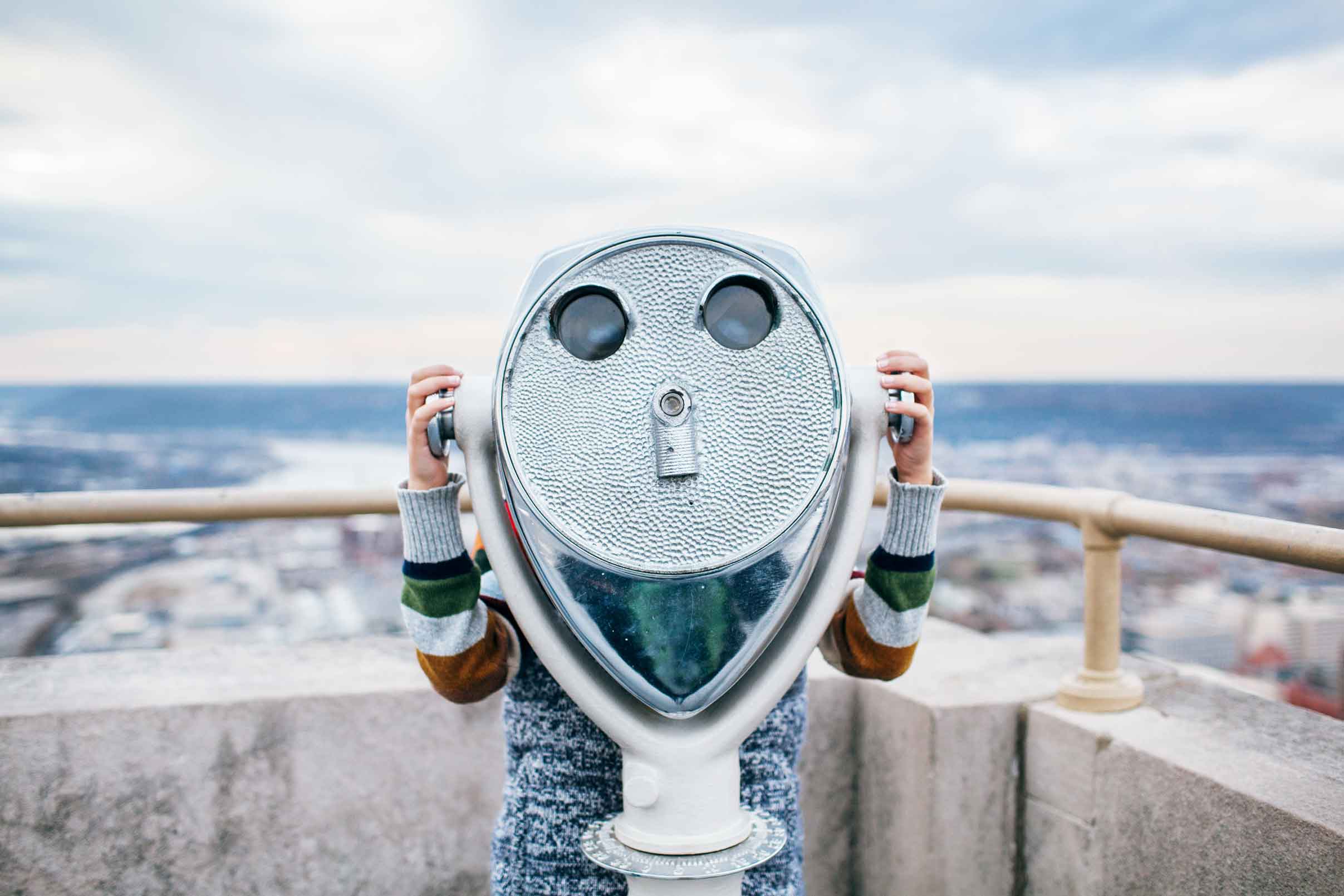 person on a rooftop looking through a tower viewer
