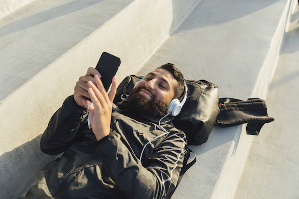 Hombre acostado en un banco mirando el telefono y escuchando musica